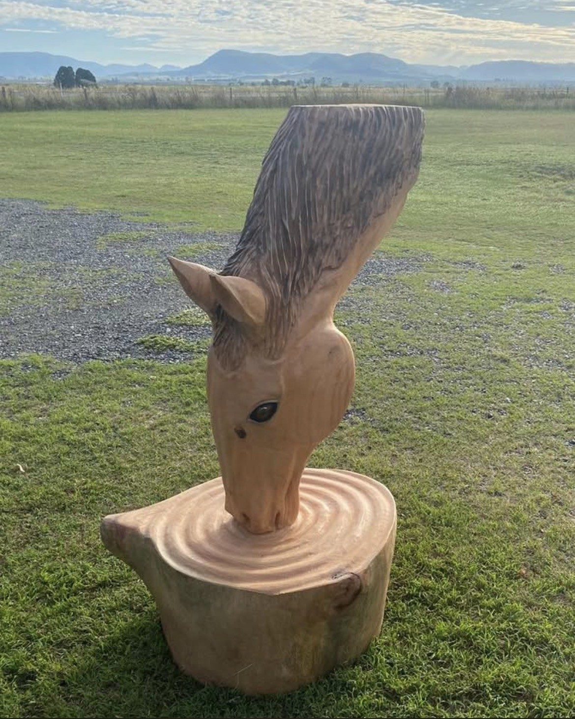 Chainsaw-carved horse head rising from a log round