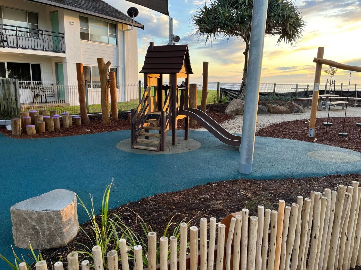 Beachside playground with timber cubby house, slide and blue rubber softfall