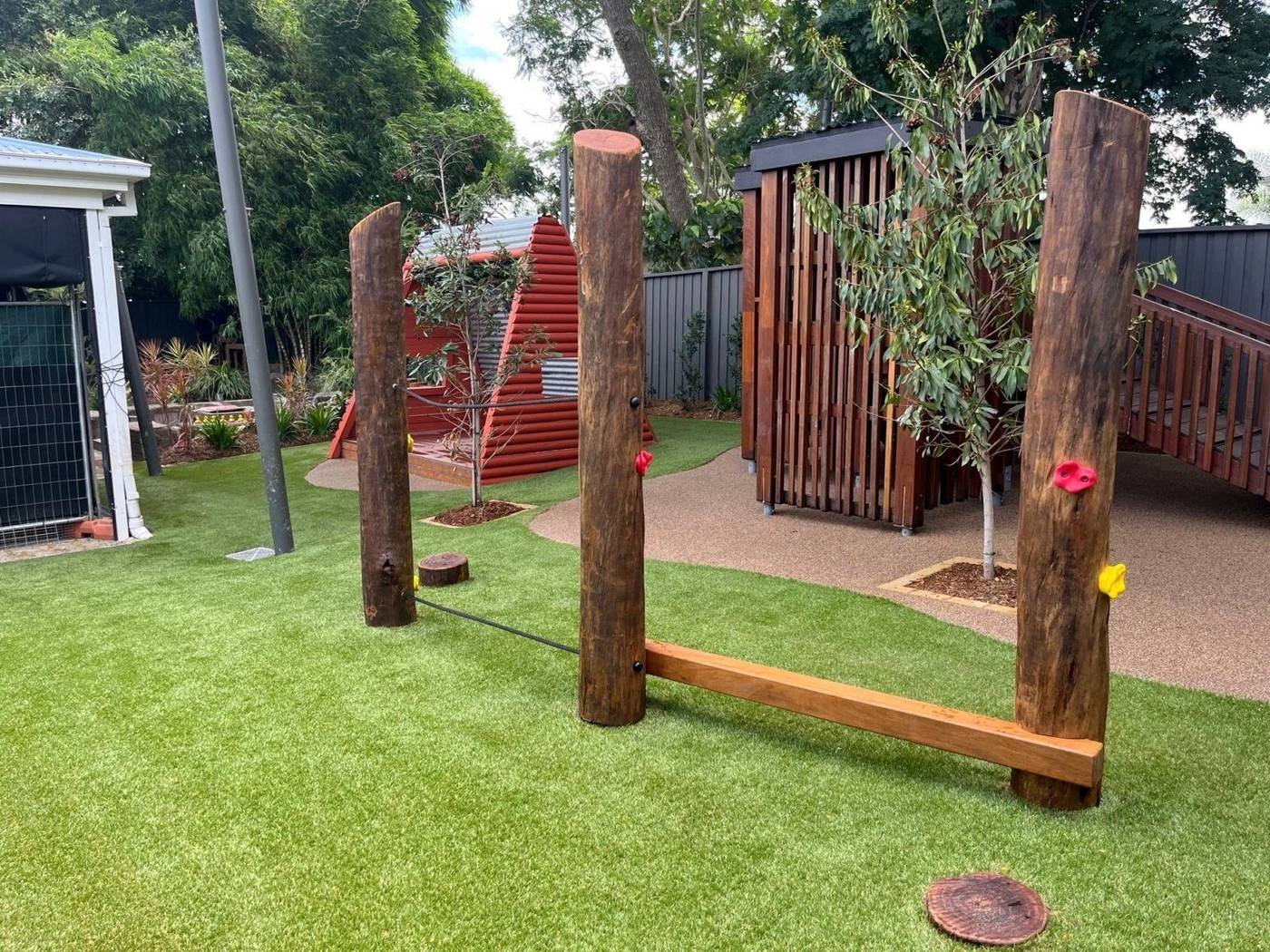 Childcare play area with log posts, climbing holds, balance beam and timber cubby