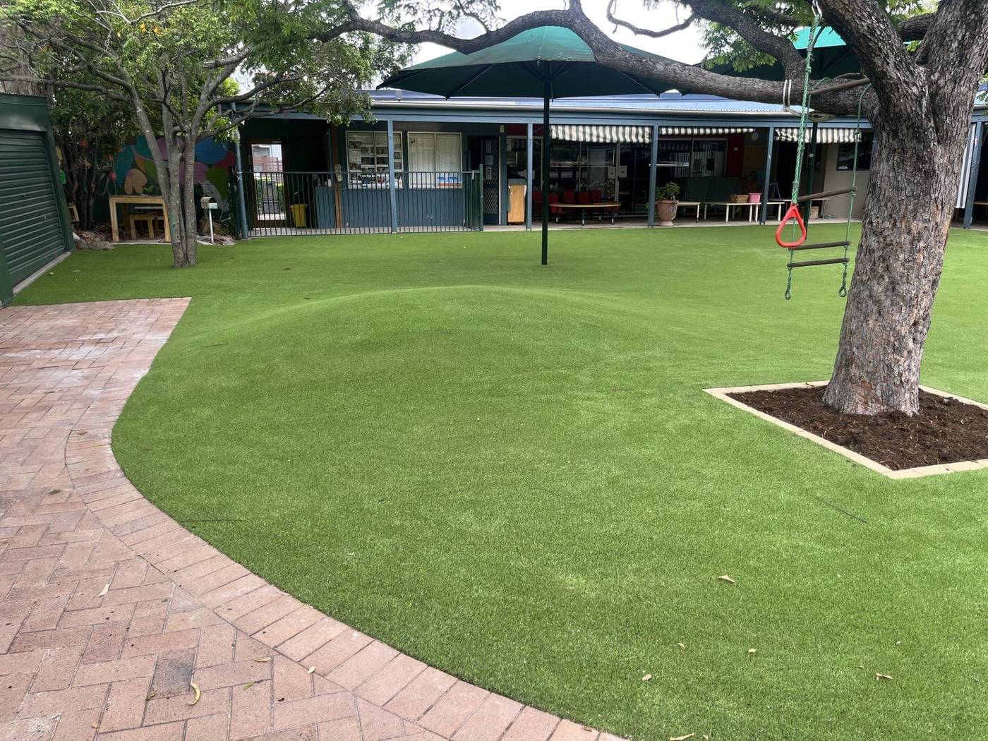 Childcare outdoor area with synthetic turf, shade sail and tree swing