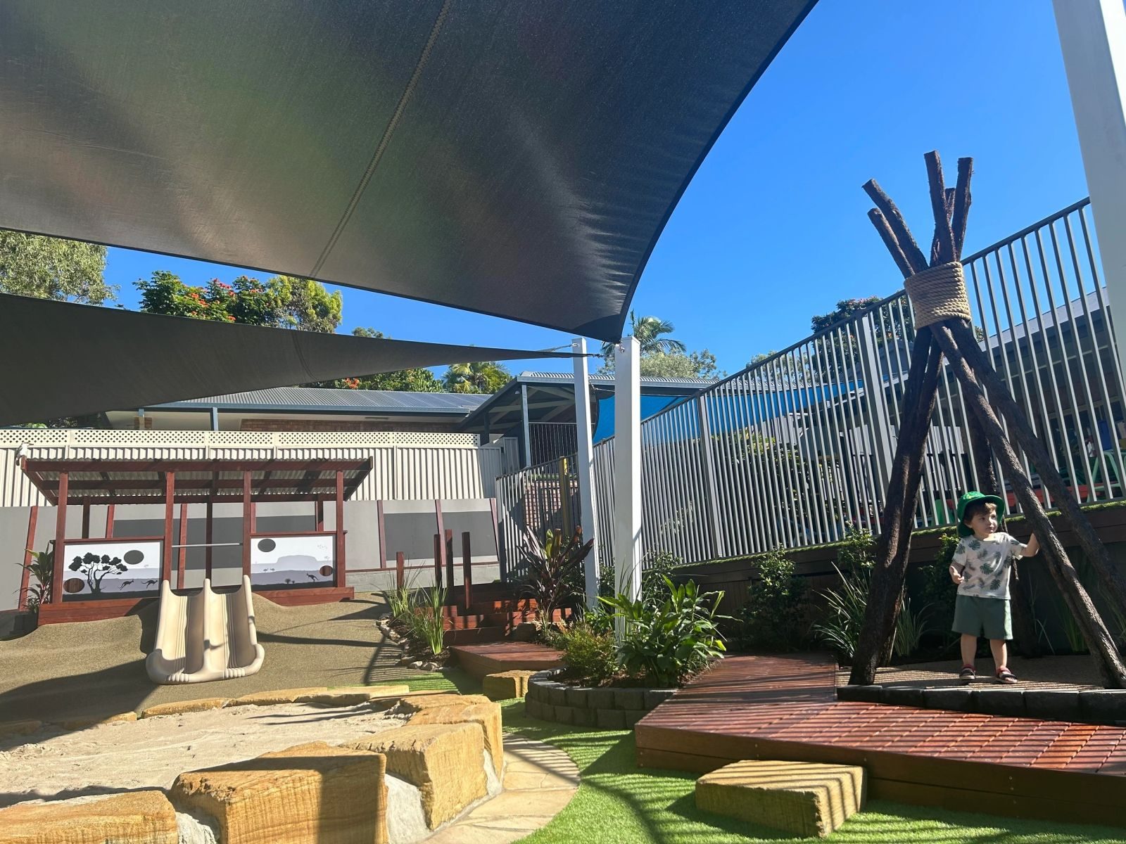 Childcare playscape with shade sails, timber teepee, sandstone stepping stones and synthetic turf